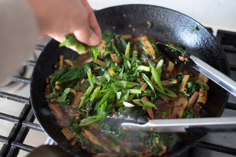 Stir-fried Swiss chard is combined with sliced green onion.