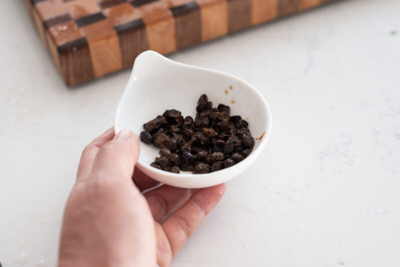 Fermented black beans (douchi) is collected in a small bowl.