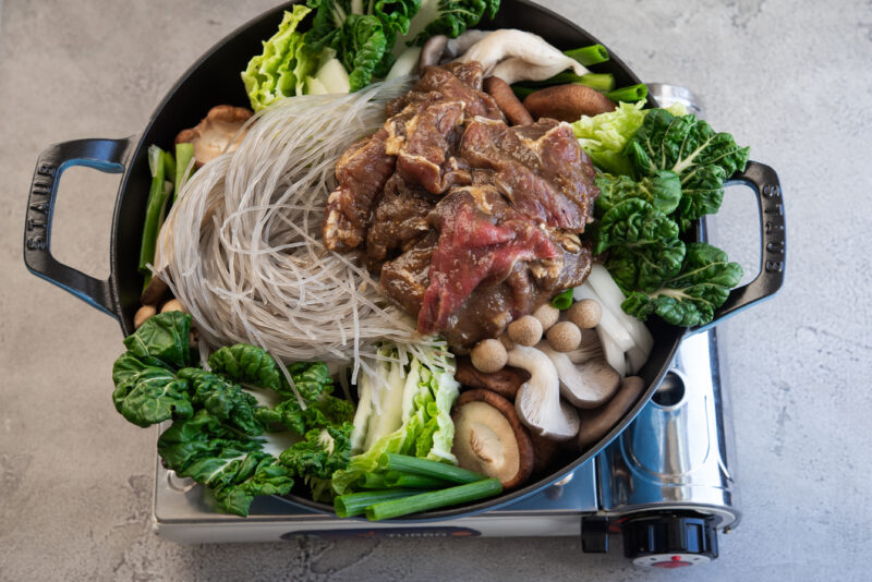 A wide pan filled with Korean beef and vegetable is getting ready to cook on the portable stove.