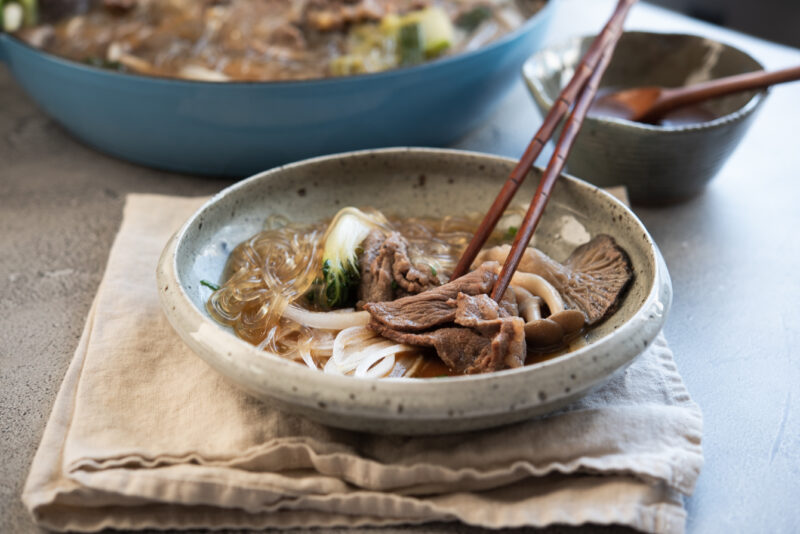 Pieces of bulgogi, mushroom are dipping in a sauce inside the serving bowl.