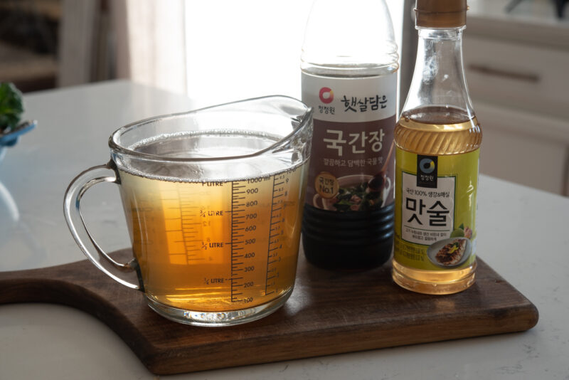 A large glass mixing cup is showing the stock mixed with soy sauce and rice wine.