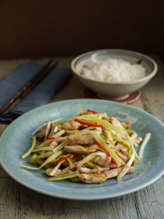 Chicken and yellow chives stir fry on a blue plate is served with a bowl of rice.