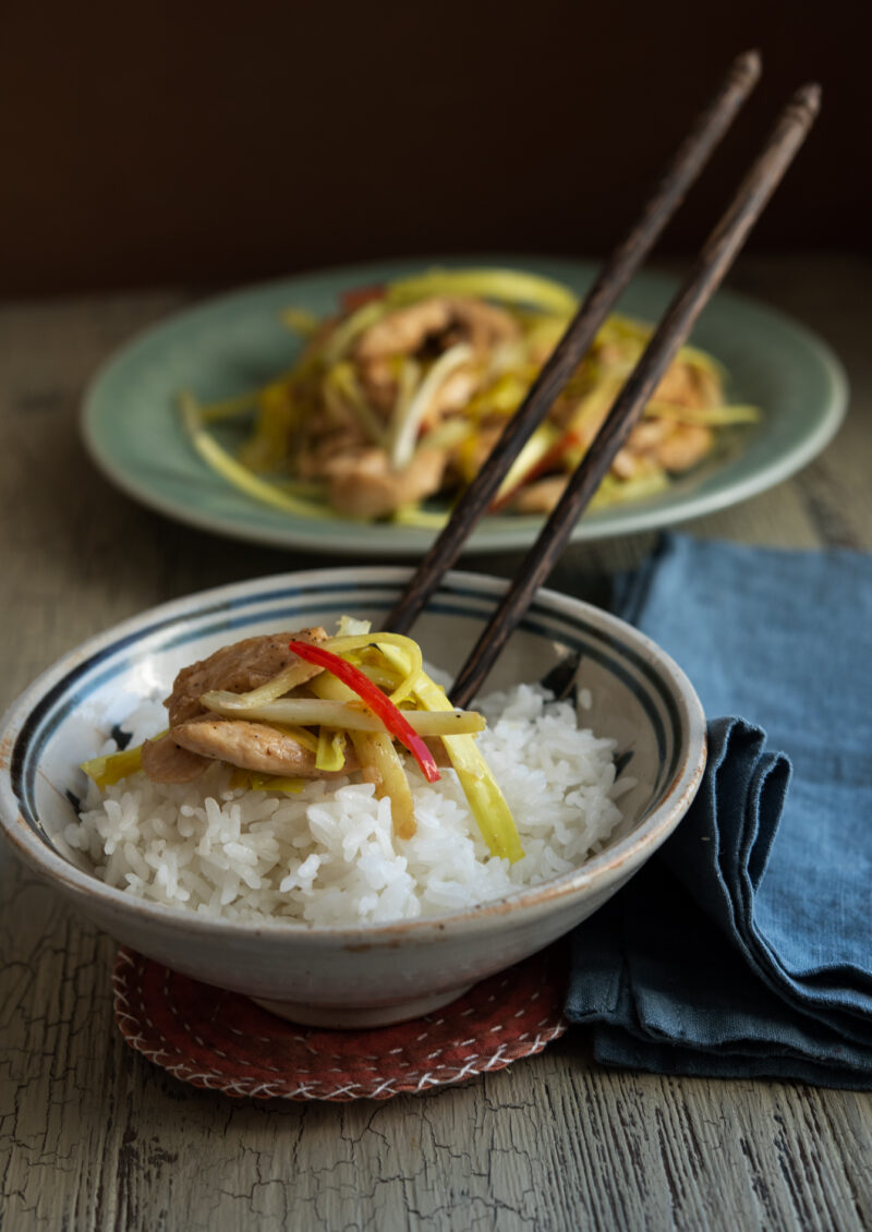  A small portion of chicken and yellow chive stir fry is placed on top of rice in a bowl with chopsticks.