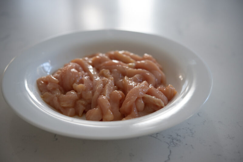 Thin strips of chicken breast is marinating in a bowl.