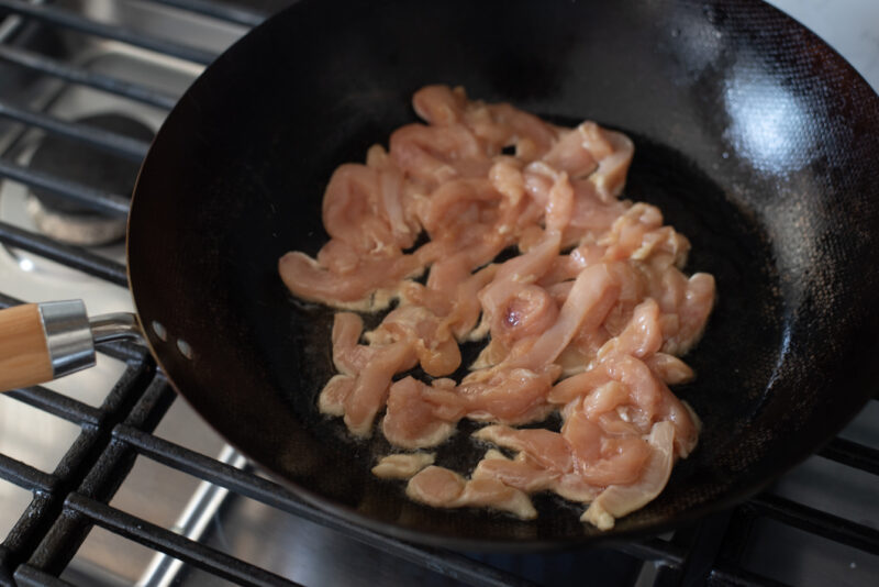 Chicken breast strips are searing with hot oil in a wok.