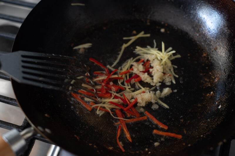 Chili, garlic, ginger slices are stir frying in a wok.
