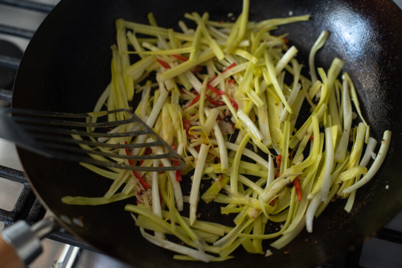 Sliced yellow chives are added to chili garlic mixture in a wok.