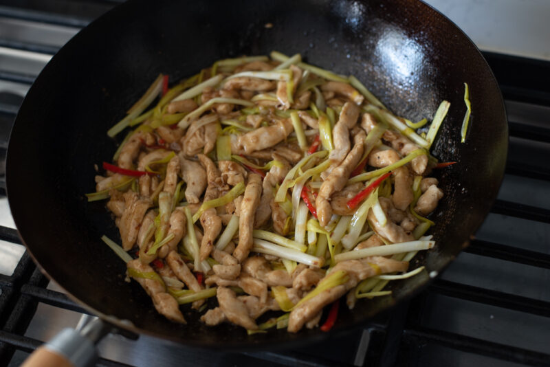chicken breast and yellow chives are stir-fried with the sauce in a wok.
