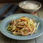 Chicken and yellow chives stir fry on a blue plate is served with a bowl of rice.