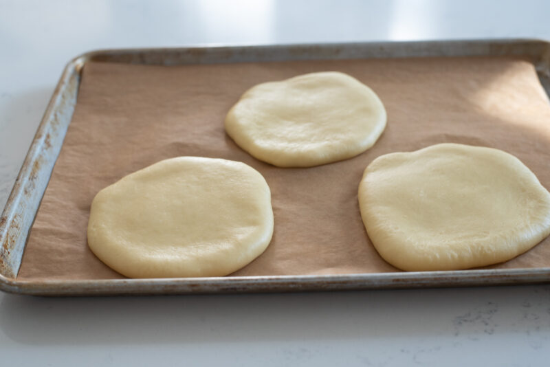Three flat round brioche dough has risen in the pan lined with parchment paper.