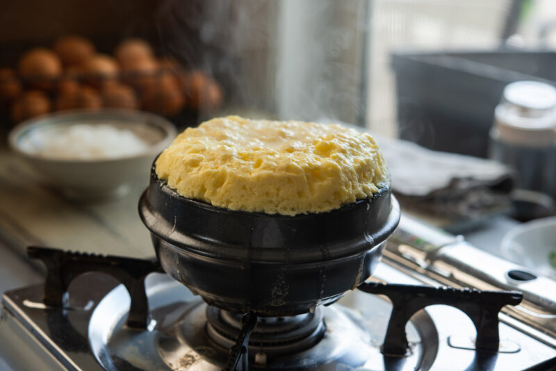 Volcano steamed egg risen well above the rim of pot with steam coming up.
