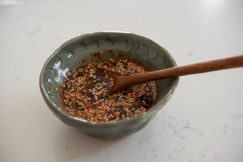 Korean soy chili sauce is combined in a small green bowl with a spoon.