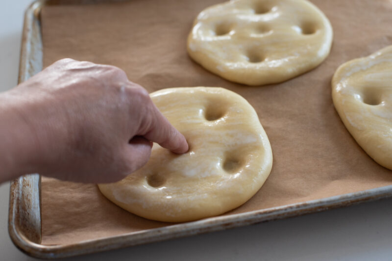 A finger is poking the risen brioche dough to make several indentation on the surface.