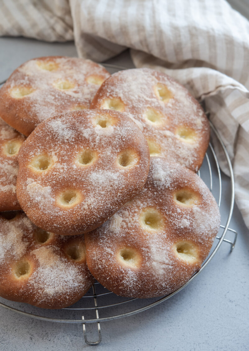 Several flat brioche tart coated with sugar are collected on a round cooling rack.