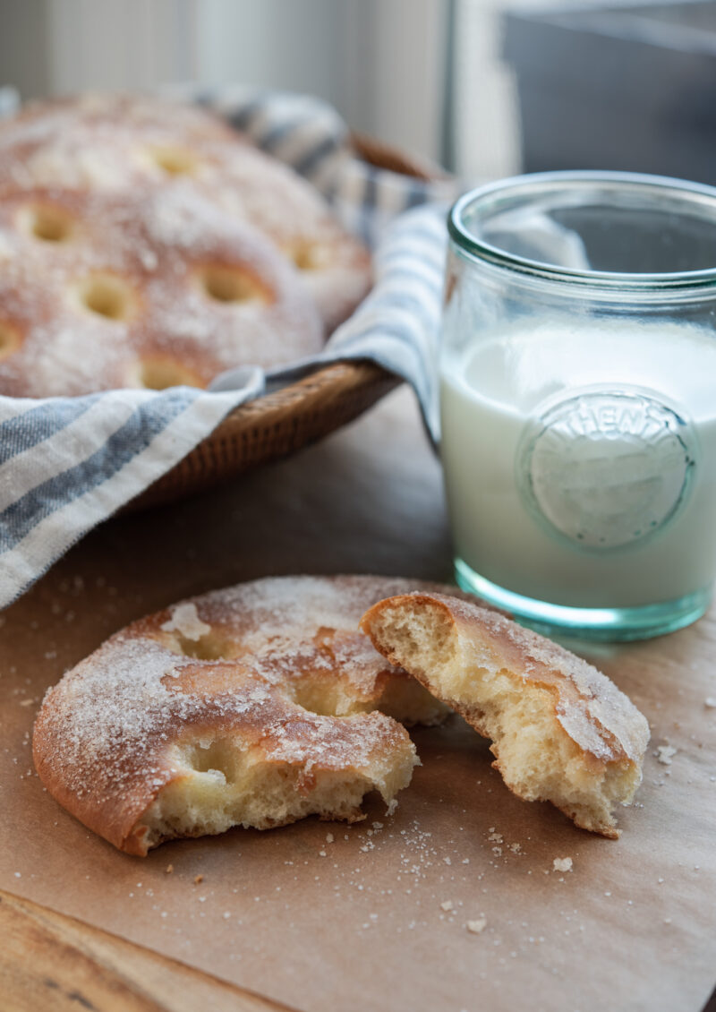 Torn brioche buns sprinkled with sugar is served with a glass of cold milk.