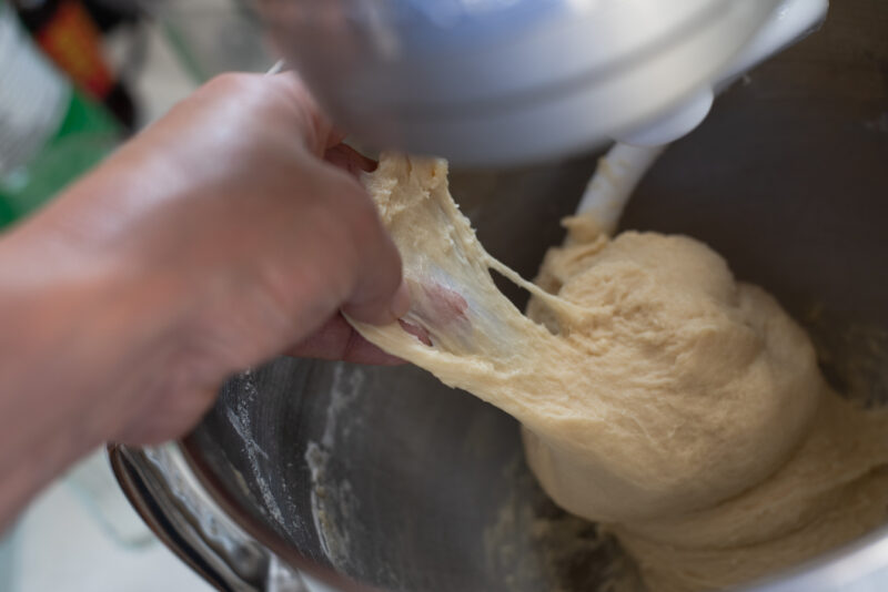 Brioche dough shows a translucent window pan test by hand.