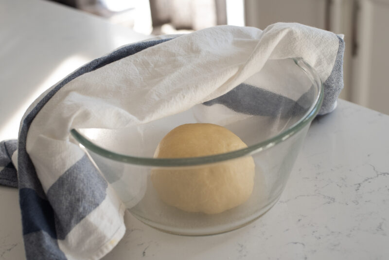 A ball of brioche dough is placed in a bowl covered with a kitchen clothe.