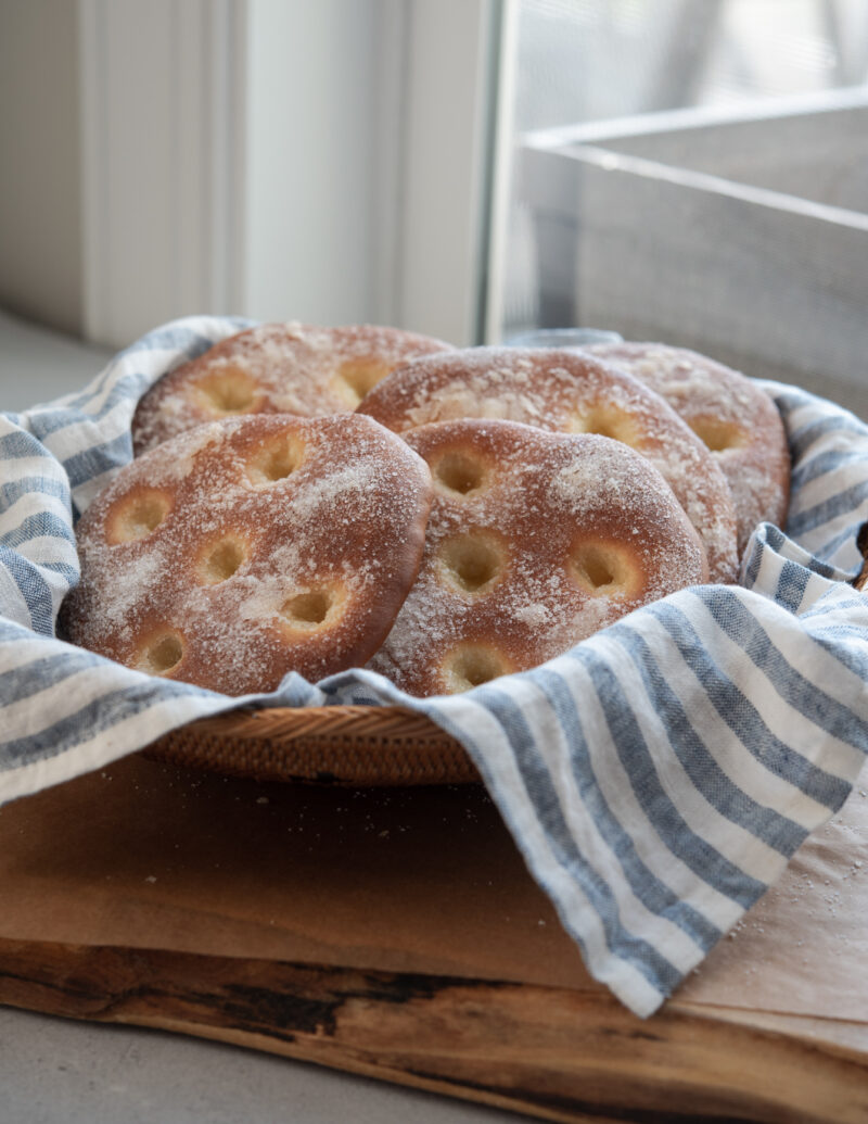Several brioche tarts are gathered in a basket lined with blue stripe napkin