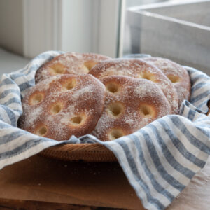 Several brioche tarts are gathered in a basket lined with blue stripe napkin.