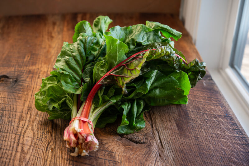 A bundle of Swiss chard with red stem is placed on a counter.