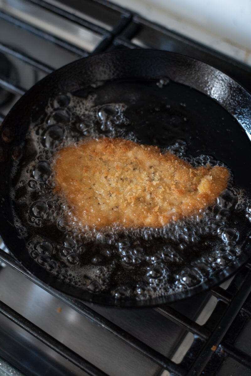 Pork tonkatsu pice is deep frying into golden brown in a hot bubblling oil.