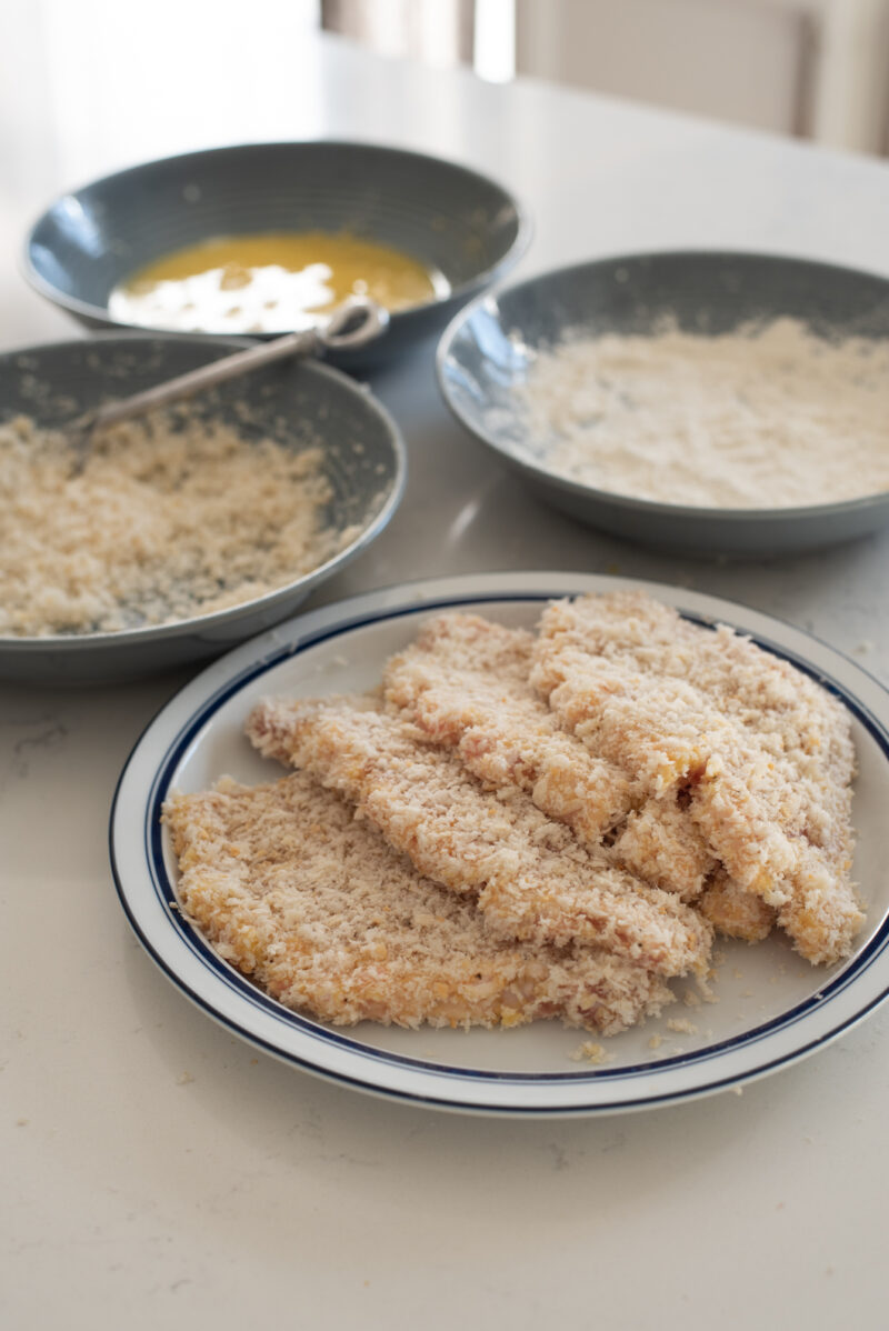Pork slices coated with flour, egg, and panko breadcrumbs are stacked in a plate.