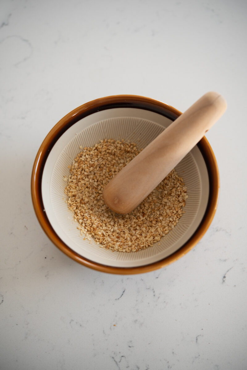 Toasted sesame seeds are crushed in a Japanese mortar and pestle.