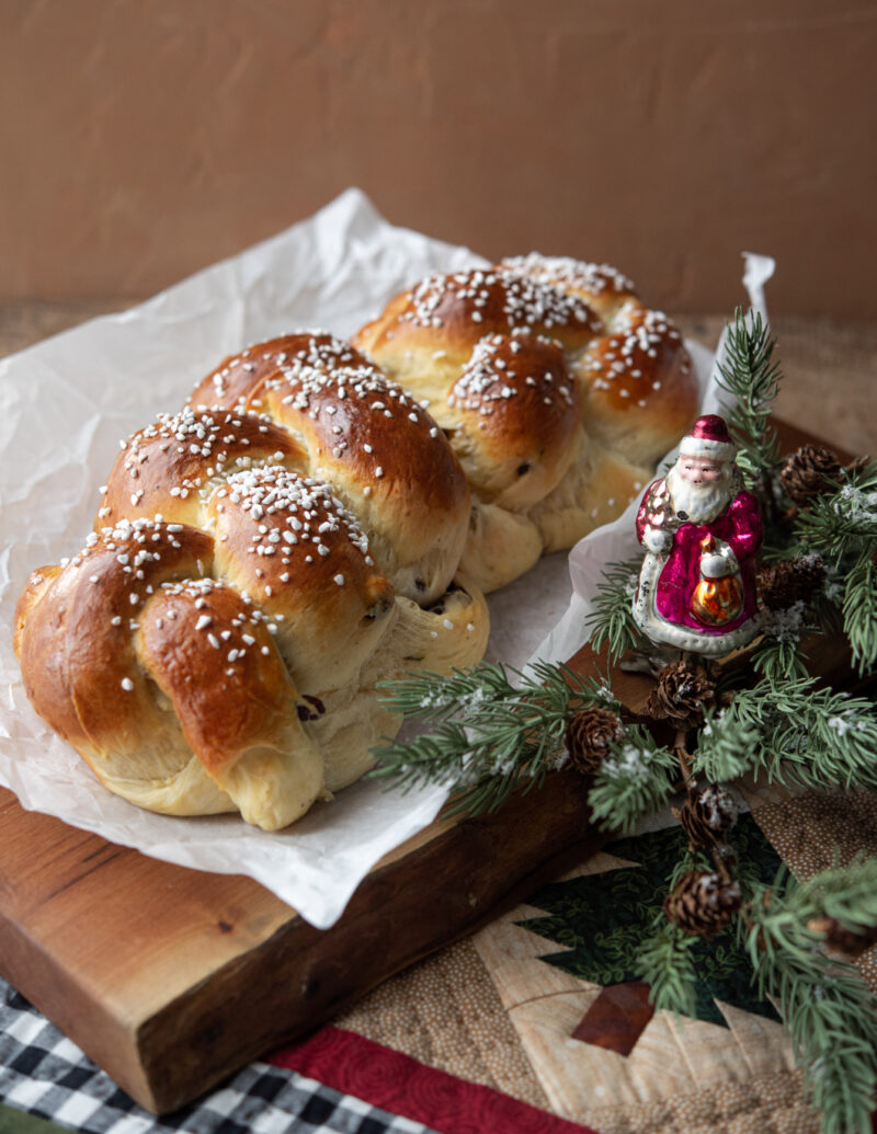 A braided loaf of cardamom bread is next to Christmas vintage Santa ornament on a greenery.