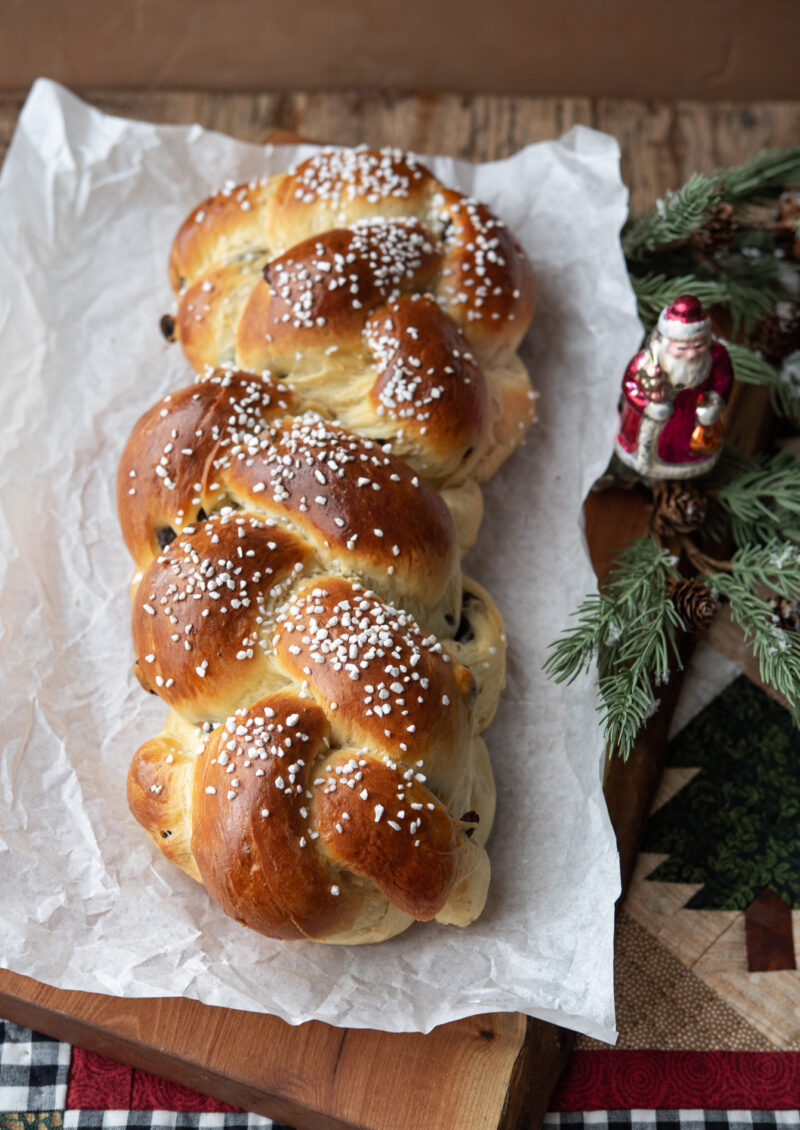 A beautiful loaf of pearl sugar topped Pulla bread is next to Holiday Santa ornament and quilt.
