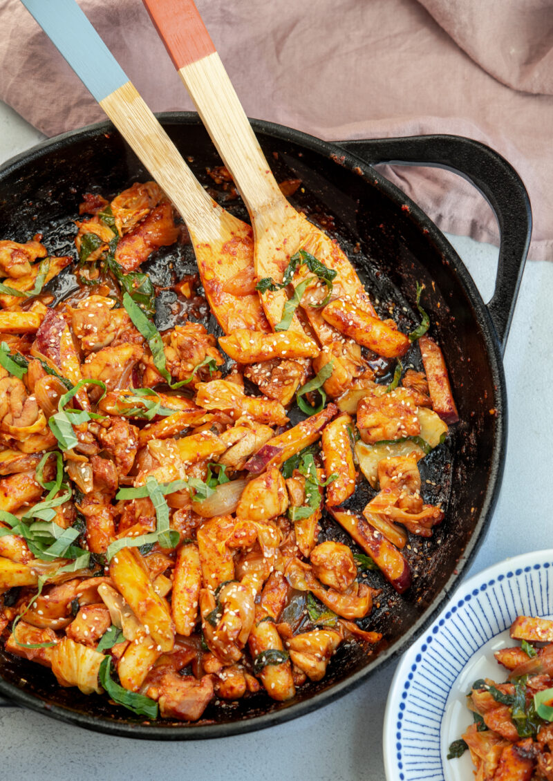 Spicy Korean chicken stir-fry with rice cake and vegetables are cooked in a large skillet.