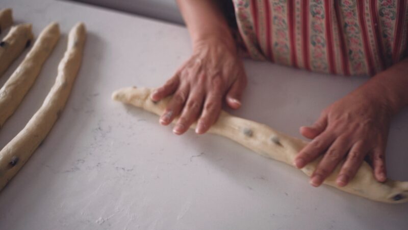 Both hands are rolling the dough pieces to make long strands.