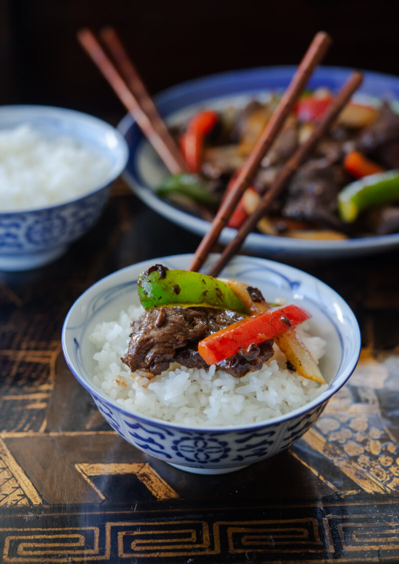 Chinese beef and pepper stir fry pieces over a bowl of white rice.