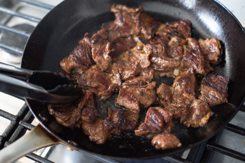 Marinated beef browning in a large skillet.