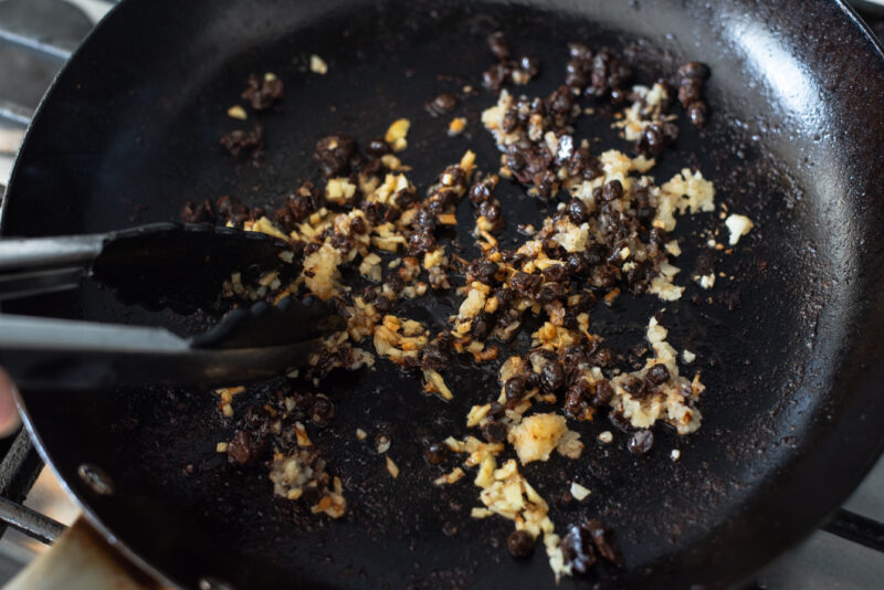 Garlic, ginger, and fermented black beans stir frying in a skillet until fragrant.