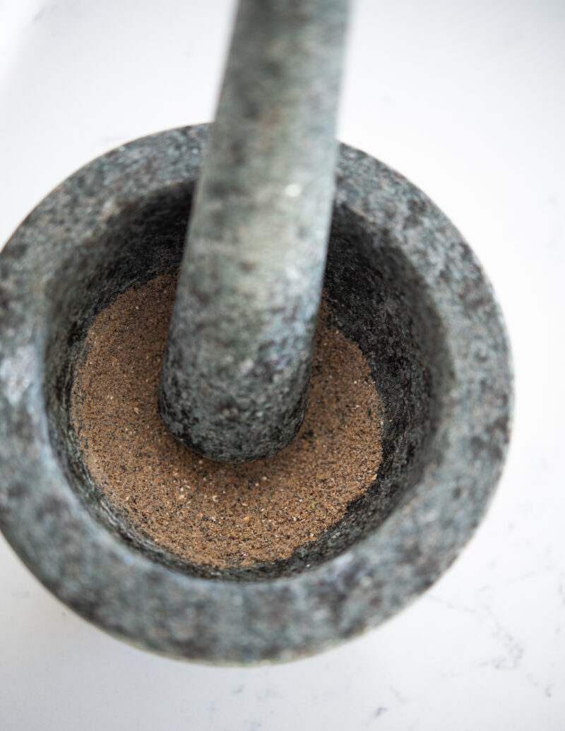 Cardamom pods are finely grounded with mortar and a pestle.