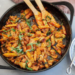 Spicy Korean chicken stir-fry with rice cake and vegetables are cooked in a large skillet.