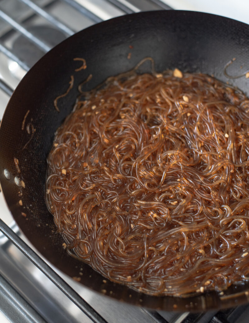 Cooked glass noodles are seasoned with soy sauce mixture.