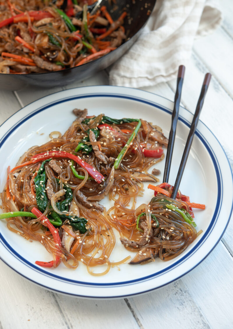 Japchae (Korean glass noodles) with vegetables served on a white plate.