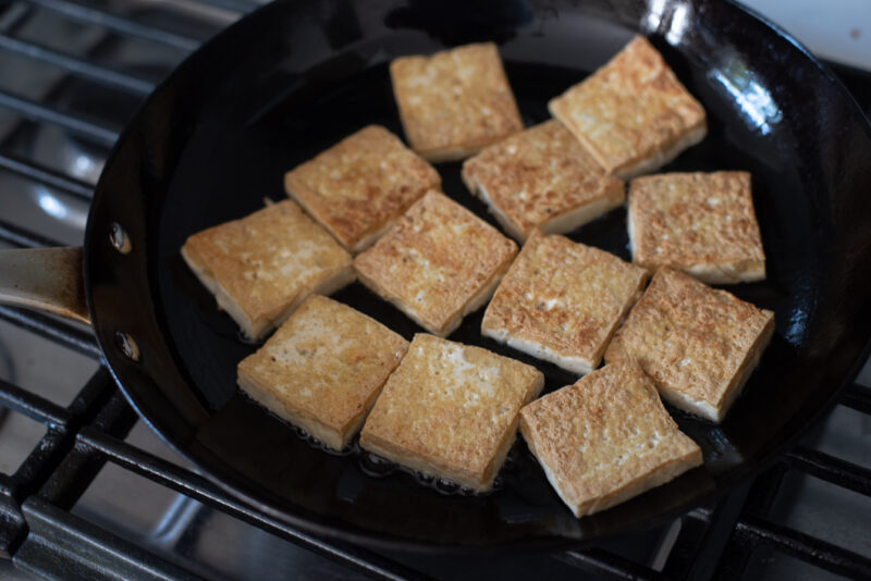 Golden crisp Korean style pan-fried tofu is cooked in a skillet.