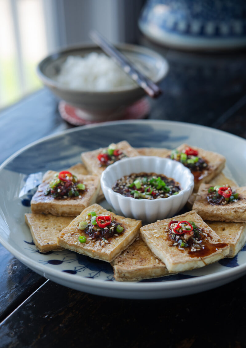 Crispy tofu slices topped with soy chili sauce on a platter.