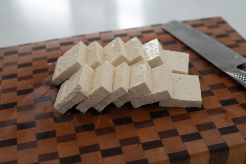 Korean firm tofu is sliced ion a cutting board.