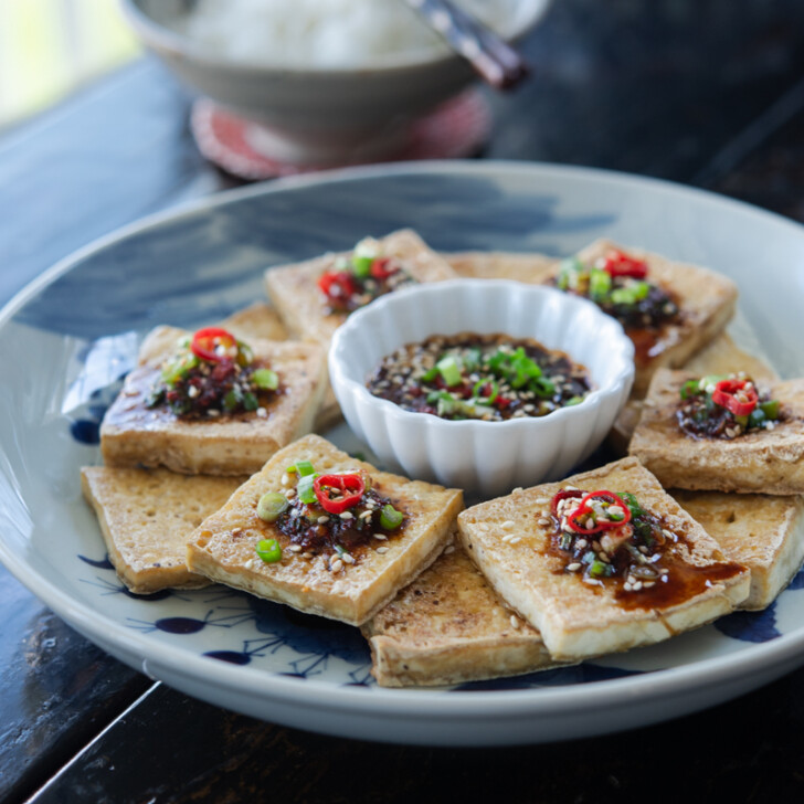 Pan seared crispy tofu slices are topped with soy chili sauce on a platter