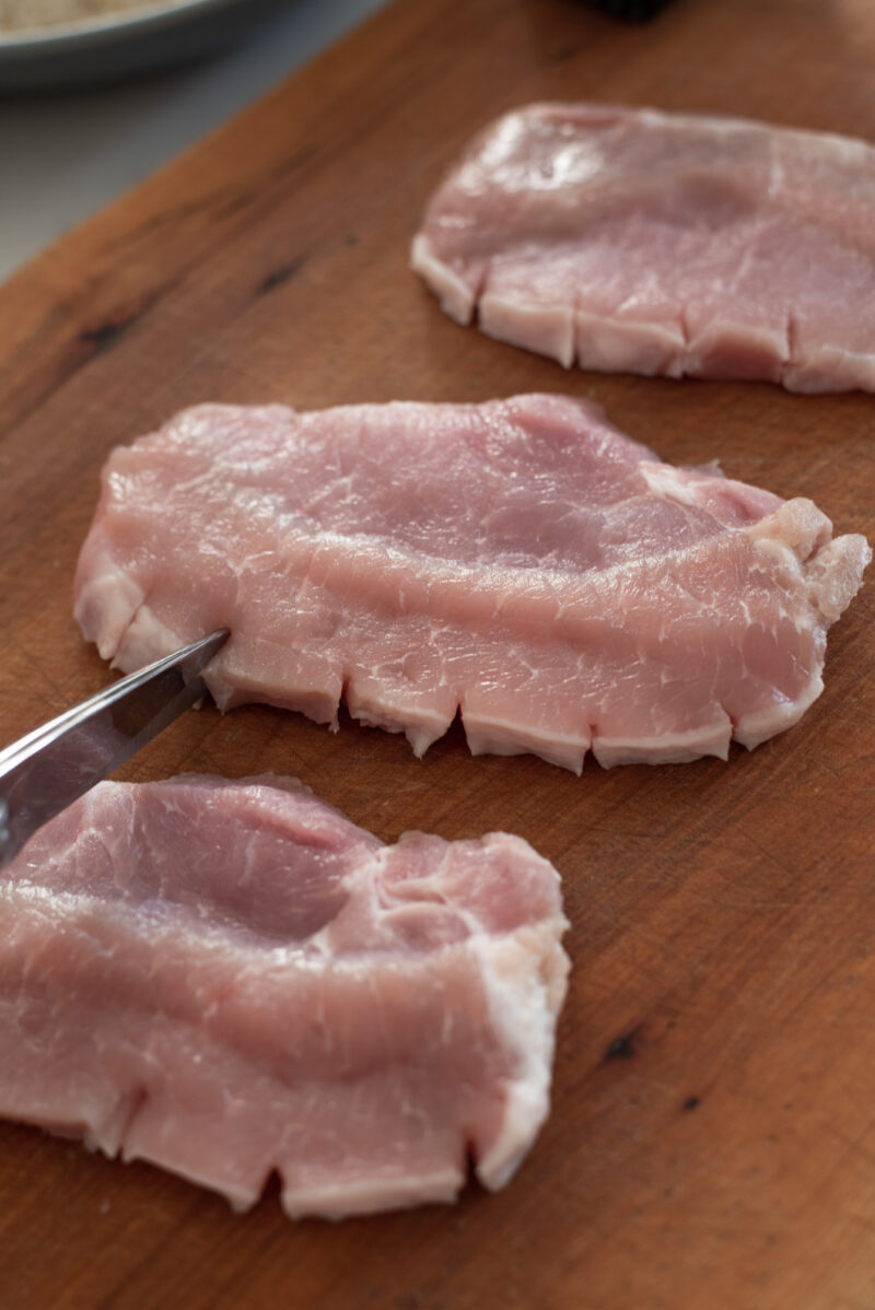 kitchen scissors are clipping the edges of pork loin slices.