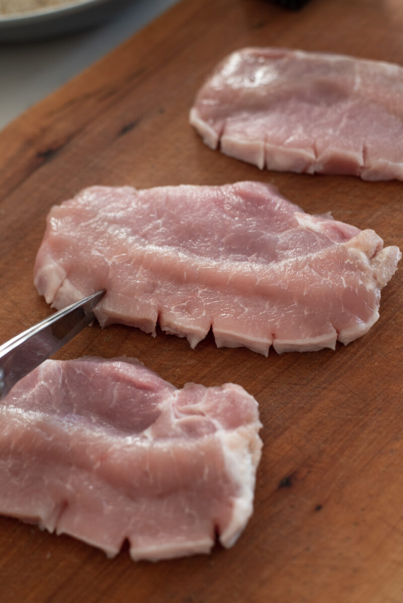 kitchen scissors clipping the edges of pork loin slices.