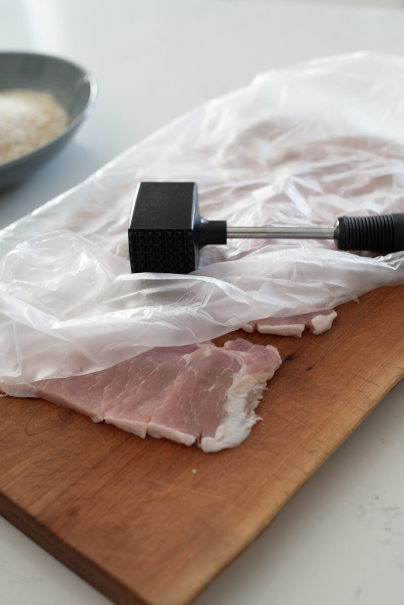 Thin pork loin slices are covered with plastic and pounded with a meat hammer.
