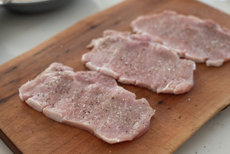 Pounded pork loin slices are seasoned with salt and pepper.