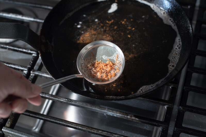 A fine mesh strainer is skimming  off the floating fried crumbs in between deep-frying.