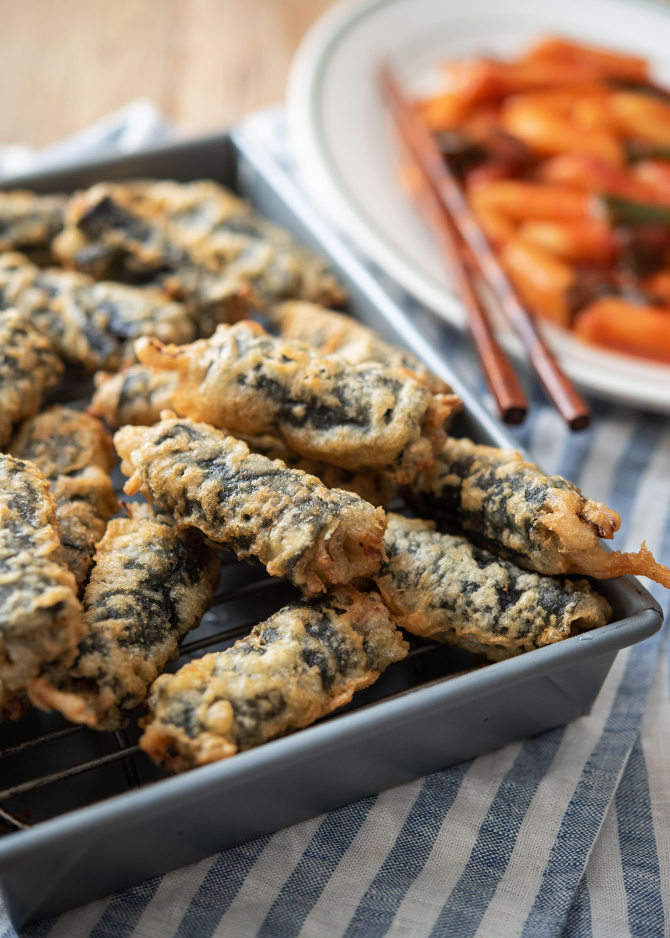 Freshly deep-fried Korean seaweed rolls are placed on a wired rack and served with tteokbokki.