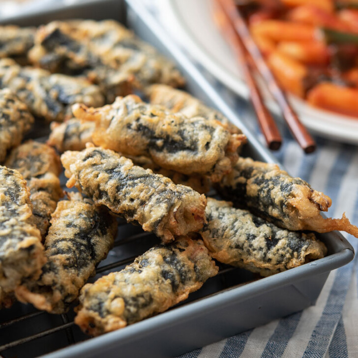 Freshly deep-fried Korean seaweed rolls are placed on a wired rack and served with tteokbokki.