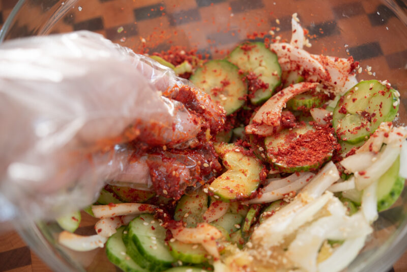 Toss Korean cucumber salad with the dressing seasoning by hand.